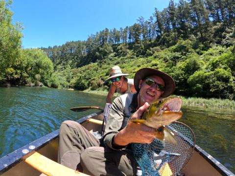 Two anglers in a canoe with a large brown trout on a clear river